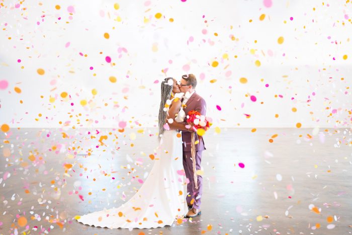 Groom Kissing Real Bride Wearing Sheath Wedding Dress by Maggie Sottero Surrounded by Colorful Confetti