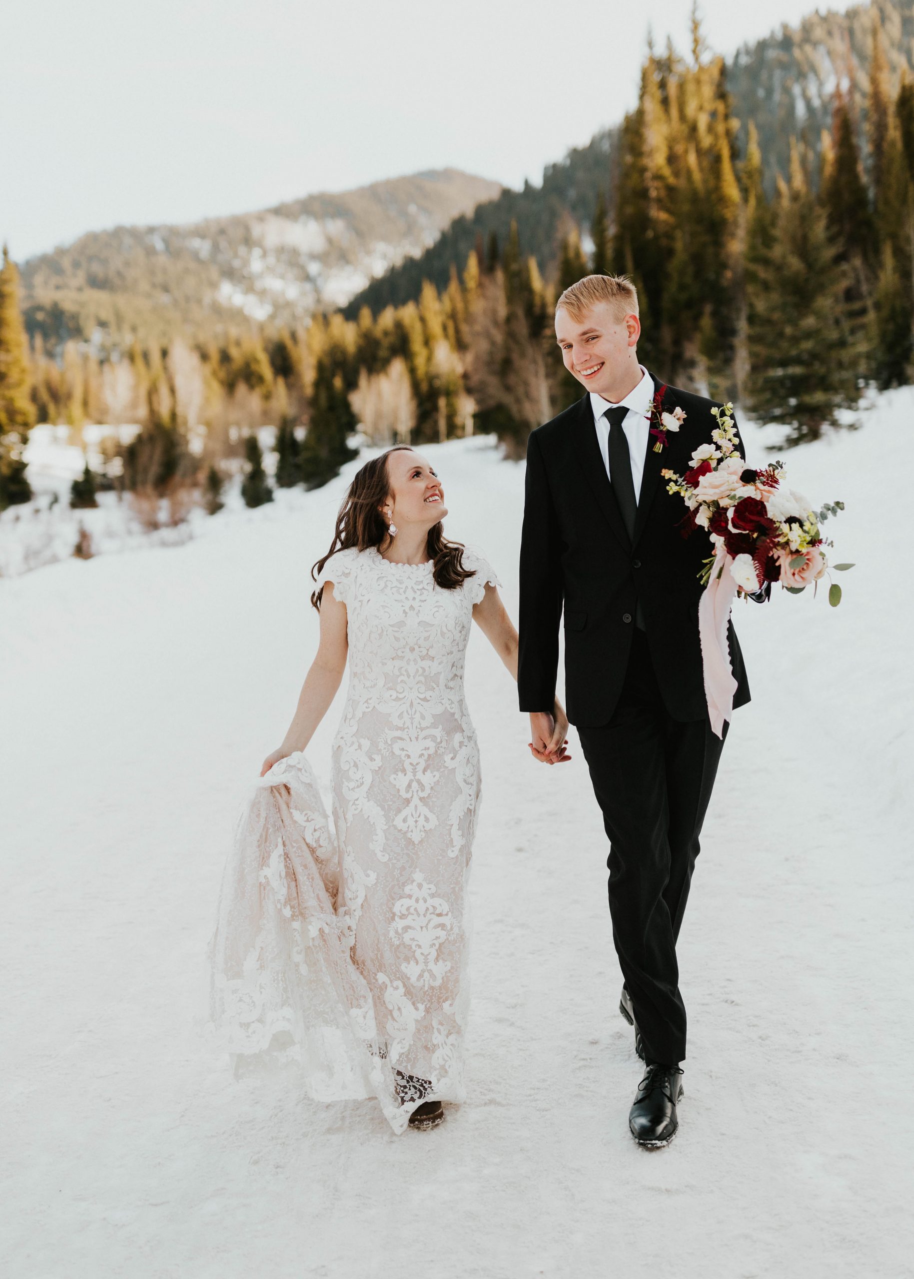 Vraie mariée portant une robe de mariée en dentelle rustique appelée Toscane Leigh par Maggie Sottero et marchant avec le marié dans la neige