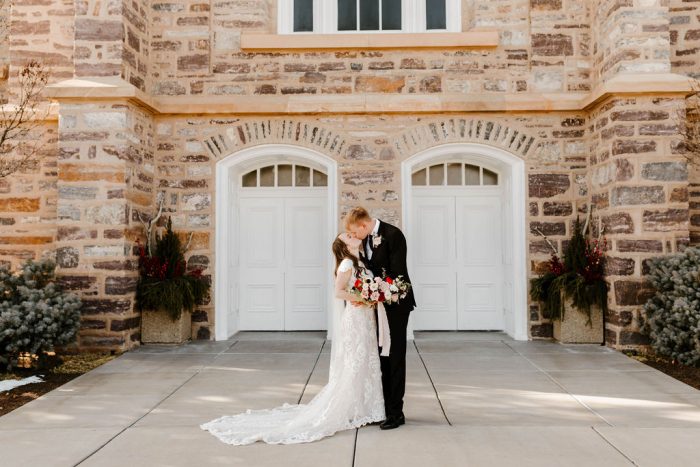 Groom Kissing Bride Wearing Rustic Lace Sheath Wedding Dress Called Tuscany Leigh by Maggie Sottero