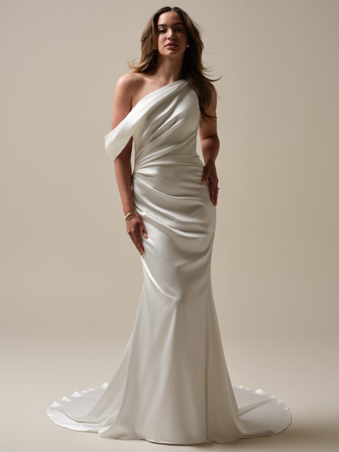 Bride wearing the Nadia sheath wedding dress featuring a one shoulder draped satin bodice, soft ruching through the waist, and a sleek fitted skirt with a gentle train.