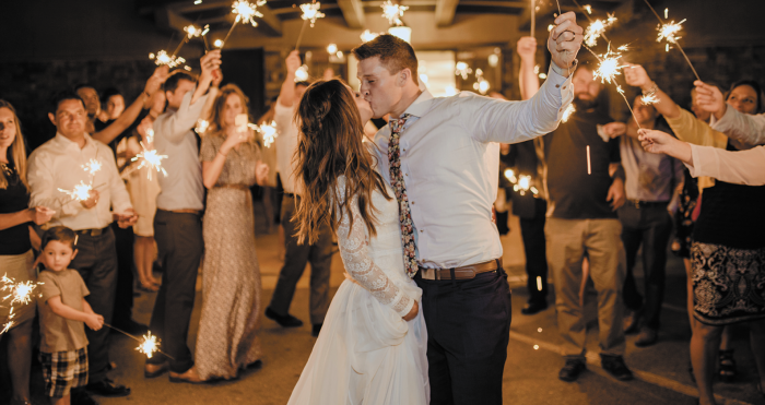 Groom Holding Sparkler and Kissing Bride Wearing Lace Wedding Dress by Maggie Sottero