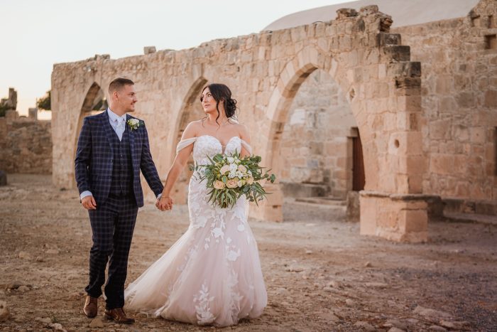 Bride Wearing Hattie Walking In Front Of Ruins With Groom