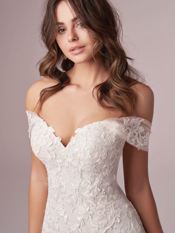 Model Wearing Off-the-Shoulder Floral Sheath Wedding Gown Called Florina by Rebecca Ingram