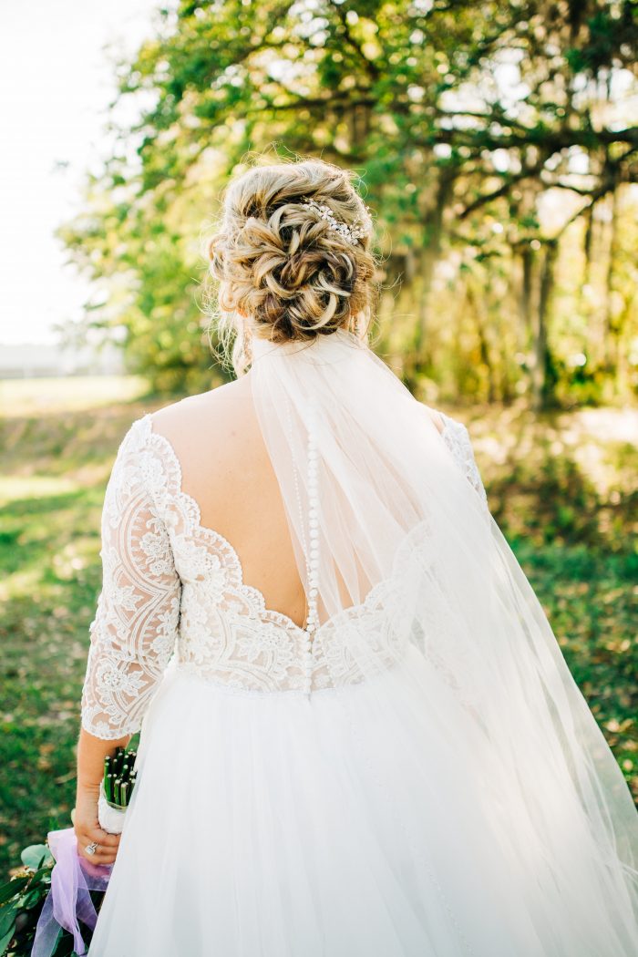 Plus Size Bride From Back Wearing Scallop Lace Off the Shoulder Wedding Dress Called Mallory Dawn by Maggie Sottero and Classic Chignon with Veil