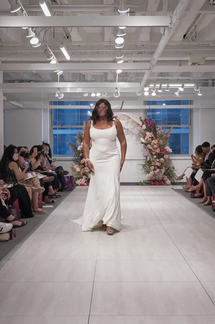 Model Walking Down the Runway at Chicago Bridal Market Wearing Plus Size Sheath Wedding Dress Called Emerald by Rebecca Ingram