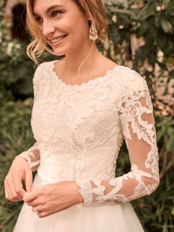Model Wearing Modest Illusion Lace Sleeve Ball Gown Wedding Dress Called Carrie Leigh by Rebecca Ingram