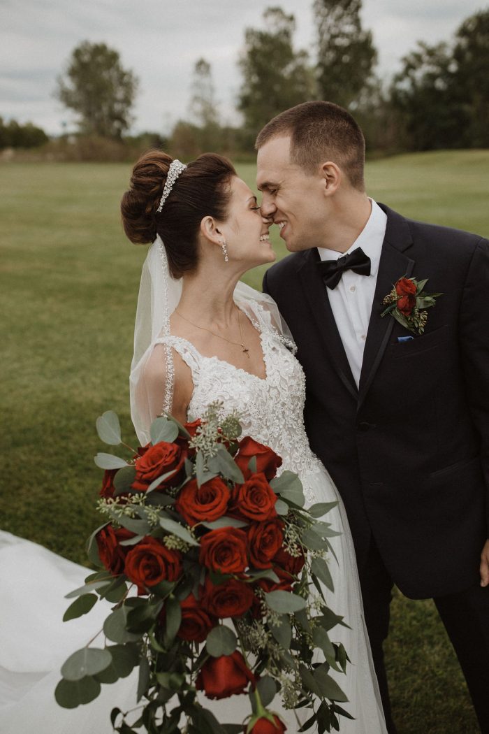 Groom Holding Real Bride While She Holds a Red Rose Bouquet