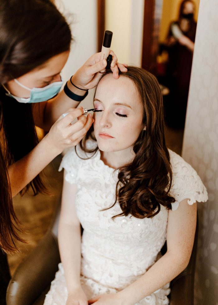 Makeup Artist Putting on Bride's Romantic Winter Wedding Makeup While Bride Wears Maggie Sottero Wedding Dress