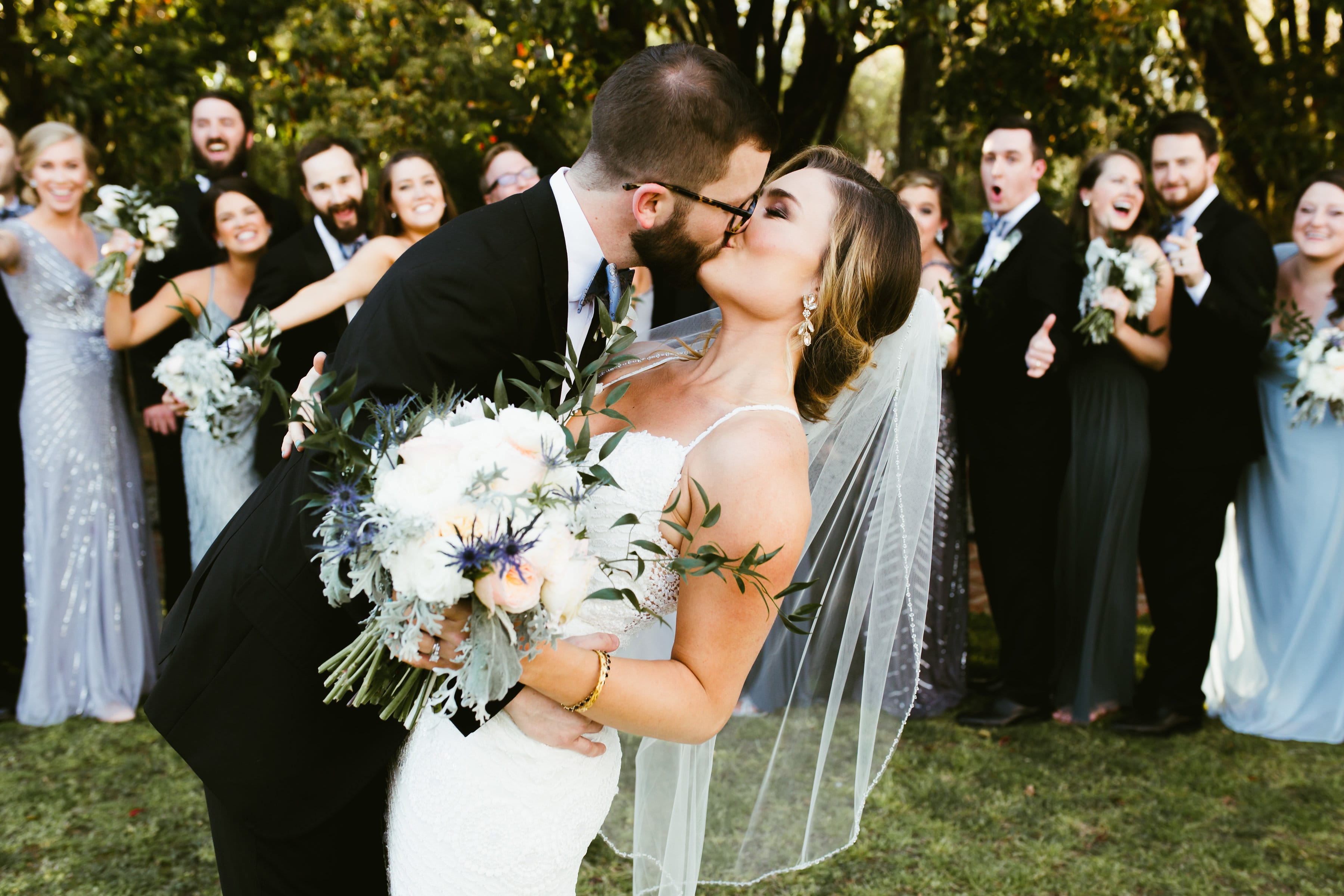 Groom Kissing Real Bride Wearing Maggie Sottero Wedding Dress While Guests Cheer in Background