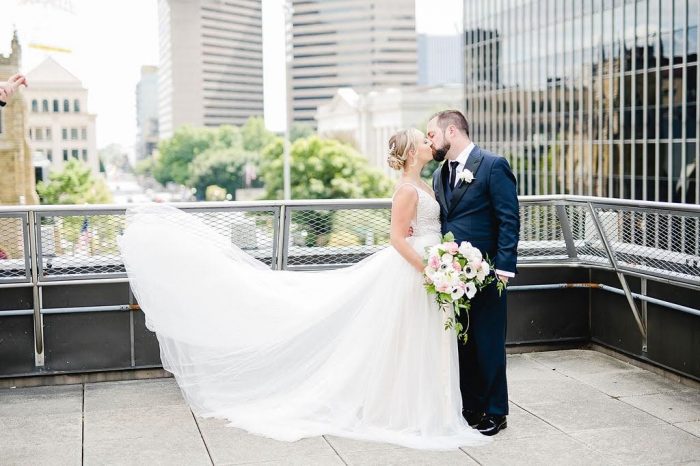 Groom Kissing Real Bride with City Backdrop While Bride's Maggie Sottero Wedding Dress Flows Behind Her