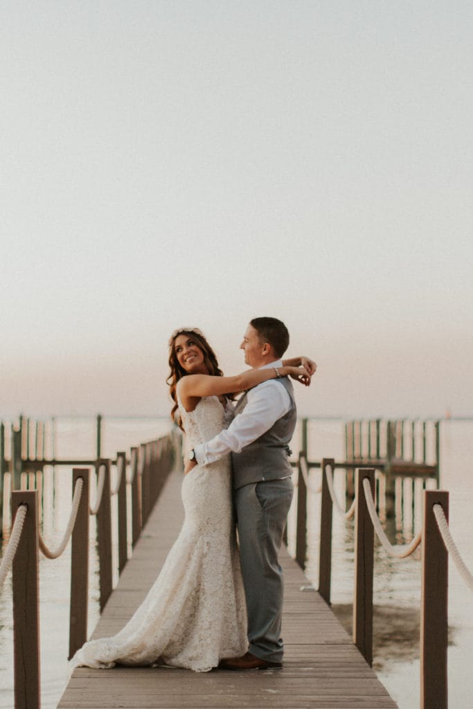 Groom on Pier Hugging Real Bride Wearing Affordable Boho Wedding Dress Called Hope by Rebecca Ingram