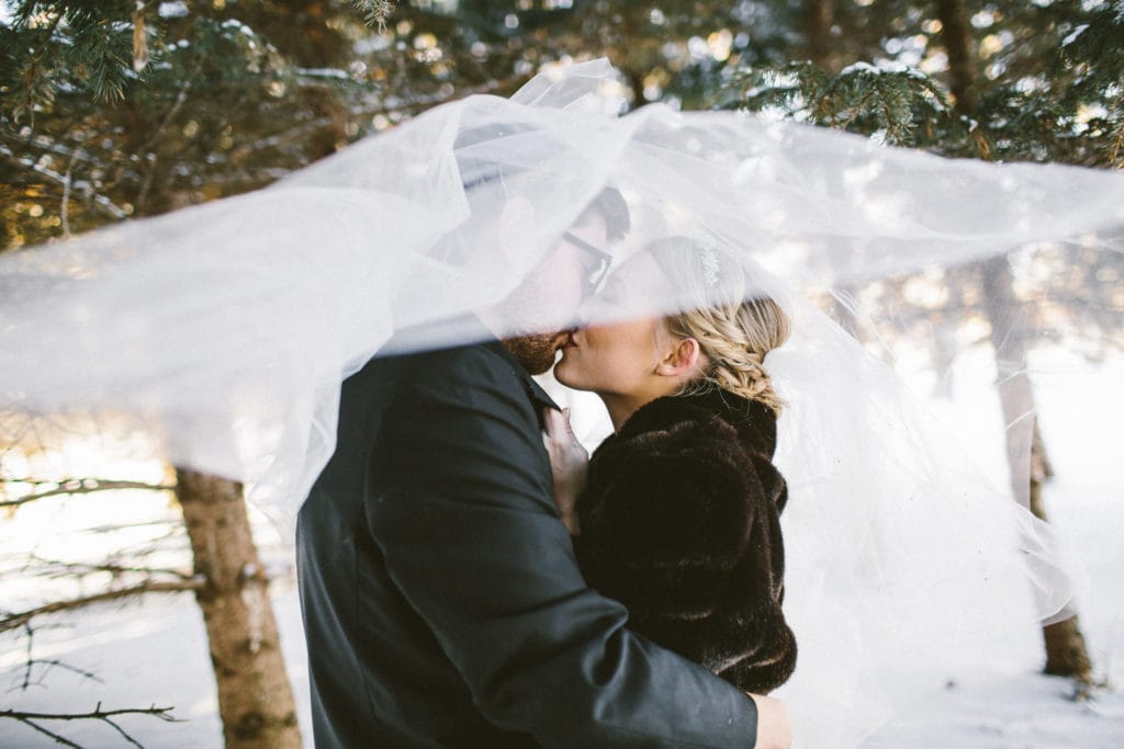 Groom in Snow Kissing Real Bride Wearing Vintage Ball Gown Wedding Dress Called Allen by Sottero and Midgley
