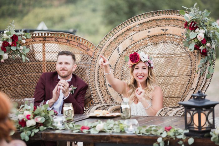Bride and Groom in wicker chairs surrounded by red and white flowers and greenery