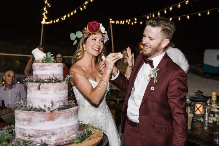 Bride wearing Watson by Maggie Sottero and Groom eating a rustic inspired cake at night