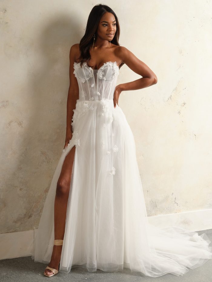 Rebecca Ingram Allison A-line wedding dress featuring a strapless corset bodice, 3D floral details, flowing tulle skirt, and thigh-high slit.