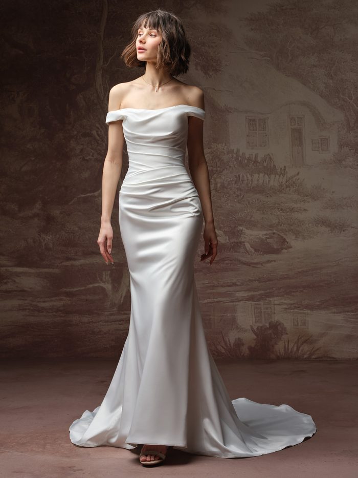 Rebecca Ingram Clementine wedding dress featuring an off-the-shoulder neckline, ruched satin bodice, fitted silhouette, and train.