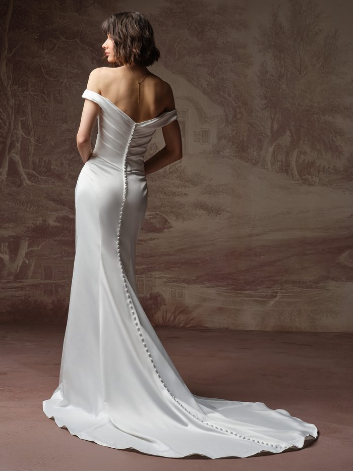Back view of Rebecca Ingram Clementine wedding dress featuring off-the-shoulder straps, ruched satin, and covered buttons.