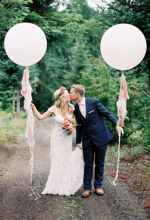 Bride wearing Alexa with Groom in the woods holding pink balloons