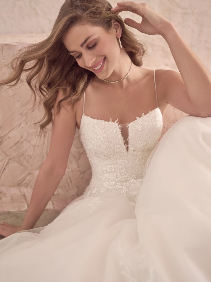 Casey ballgown wedding dress close-up showcasing intricate lace appliqués, a sheer illusion plunge, and fine spaghetti straps for an effortlessly feminine, modern bridal look