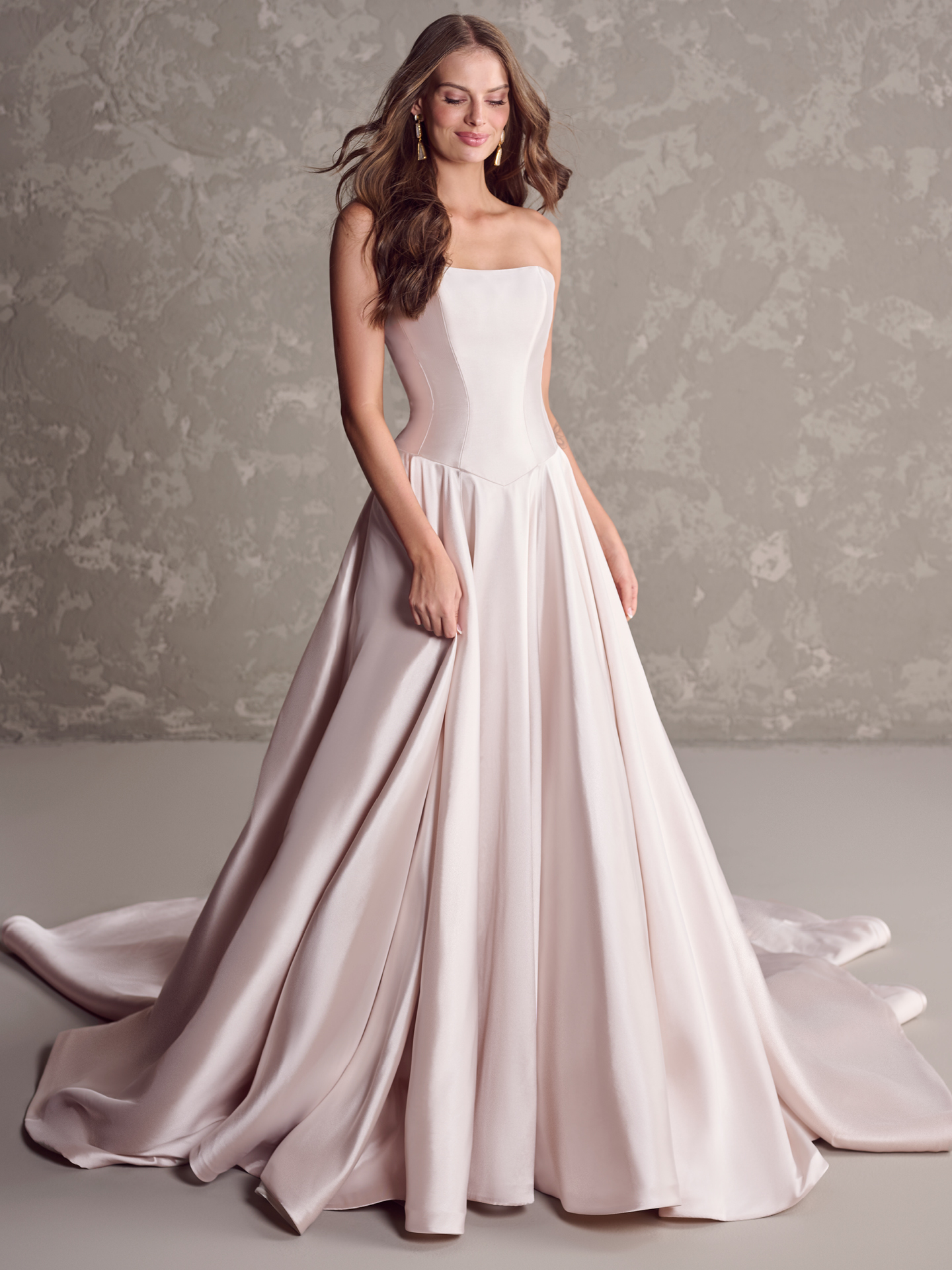 Emmanuelle ballgown wedding dress featuring a strapless straight neckline, structured satin bodice, and flowing A-line skirt with a soft blush tone and elegant drape