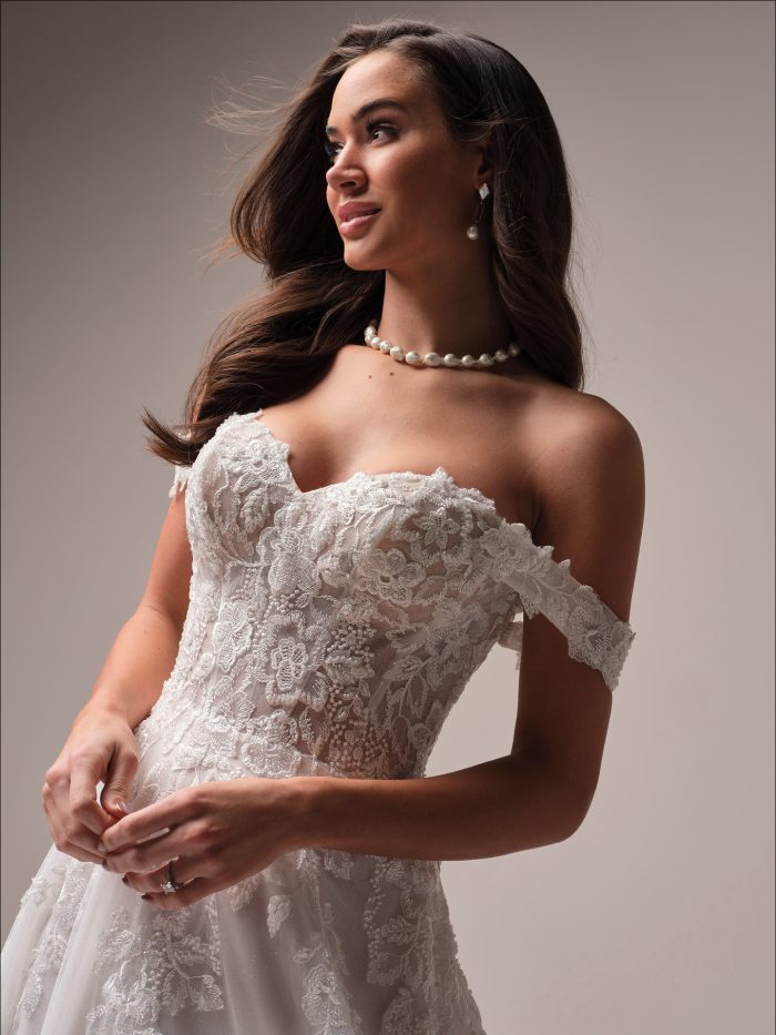 Everleigh A-line wedding dress close-up of off-the-shoulder lace bodice with intricate floral detailing, sheer illusion structure, and delicate scalloped edges
