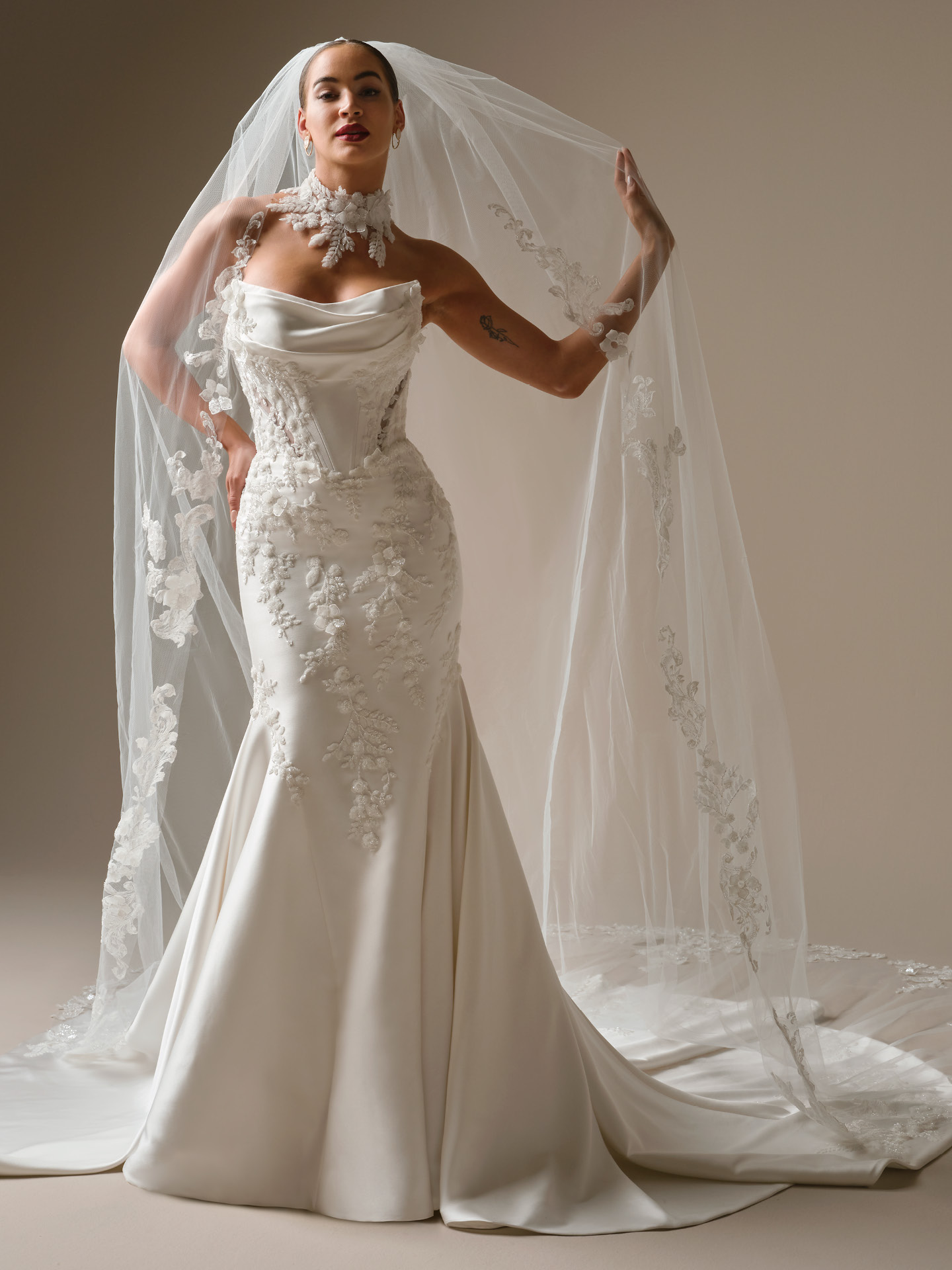 Burke fit-and-flare wedding dress featuring a strapless draped neckline, structured corset bodice, and floral lace appliqués with a fitted silhouette and cathedral veil
