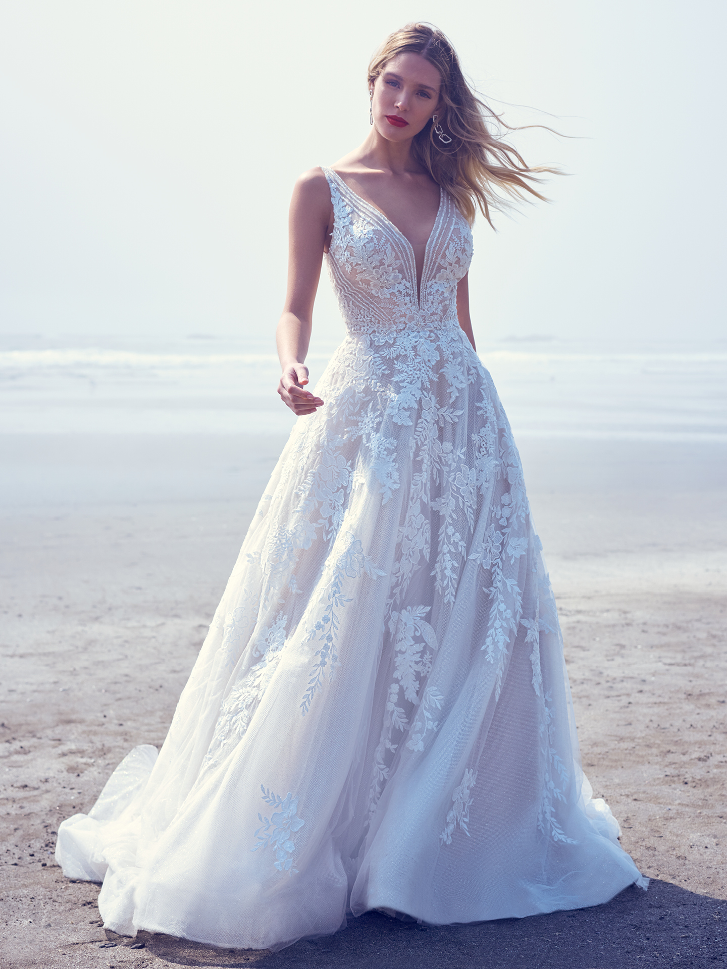 Mariée marchant sur la plage vêtue d'une robe de mariée glamour appelée Essex par Sottero et Midgley