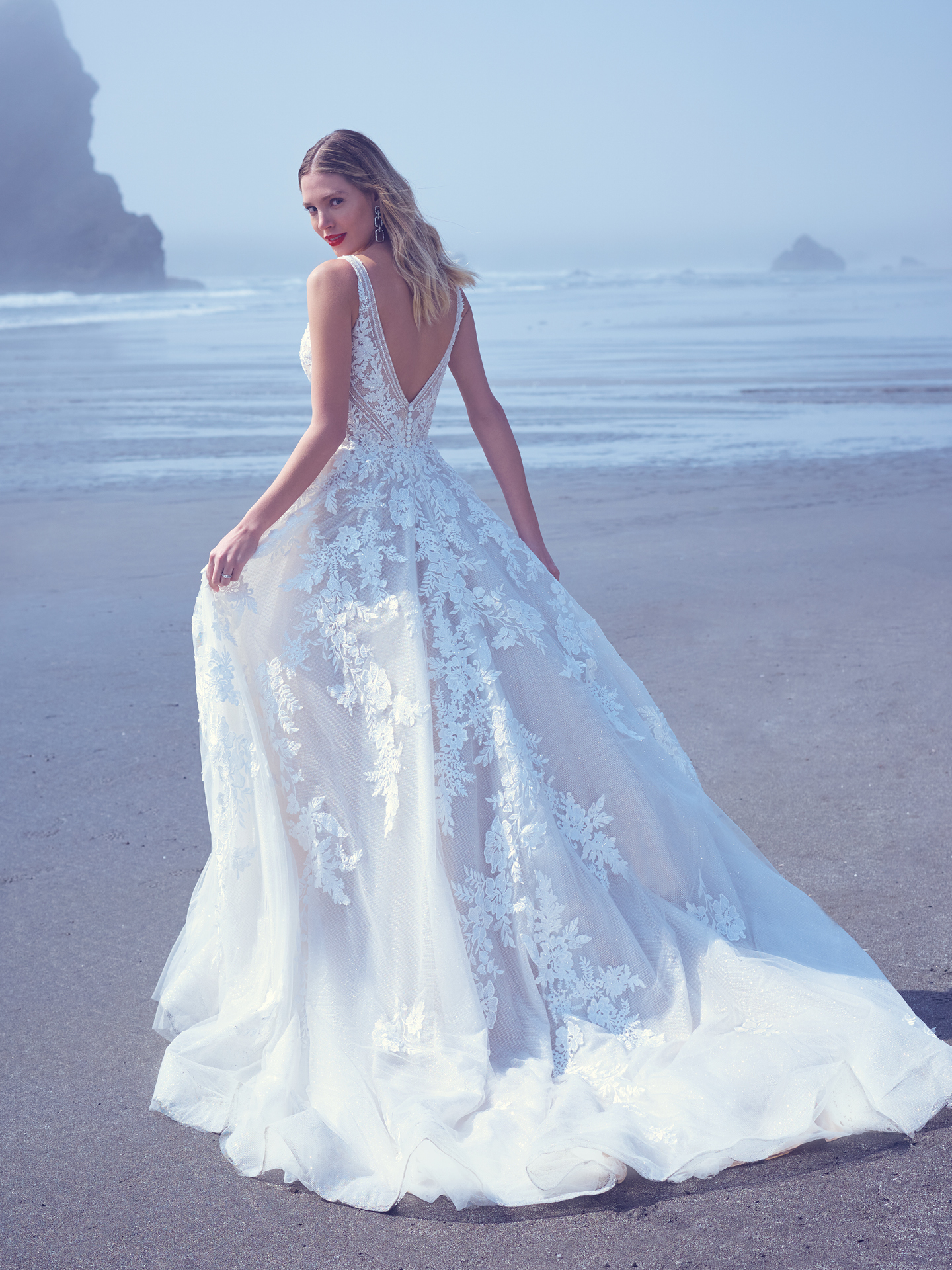 Mariée marchant sur la plage vêtue d'une robe de mariée glamour appelée Essex par Sottero et Midgley