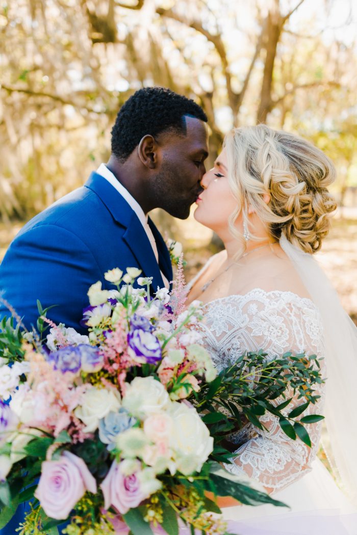Groom Kissing Real Bride with Pastel Bouquet and Wearing Lace Bridal Gown Called Mallory Dawn by Maggie Sottero