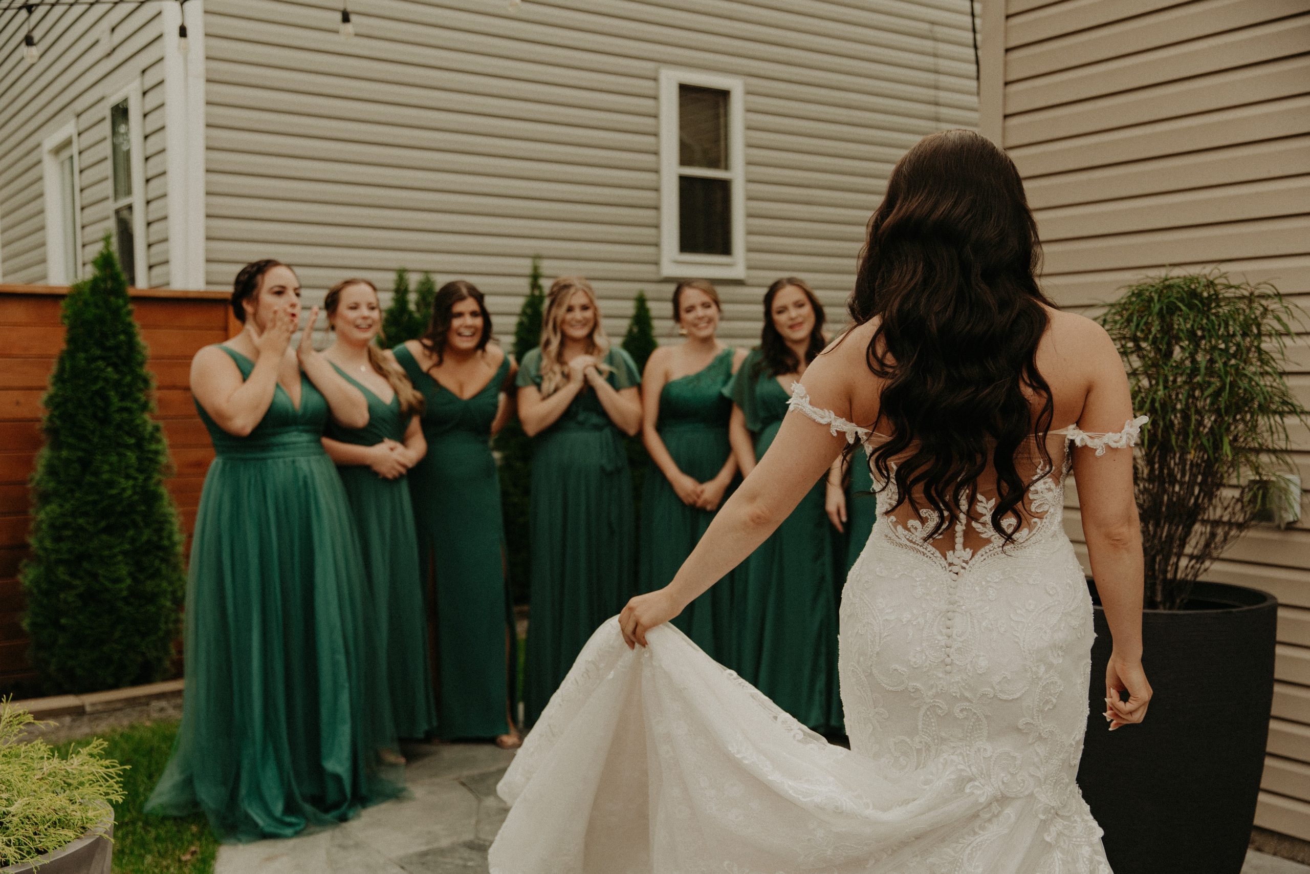 La mariée porte une robe de mariée ajustée appelée Simone par Maggie Sottero exhibant sa robe à ses demoiselles d'honneur vêtues de vert émeraude