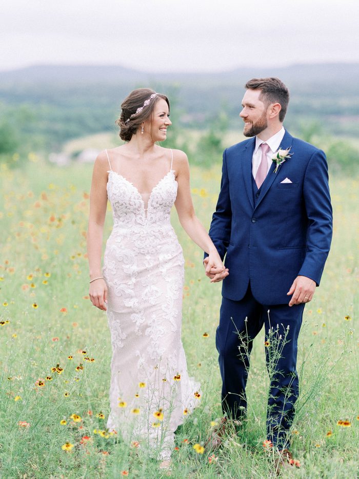 Bride Walking In Field With Groom Wearing A Wedding Gown Called Tuscany Lynette By Maggie Sottero