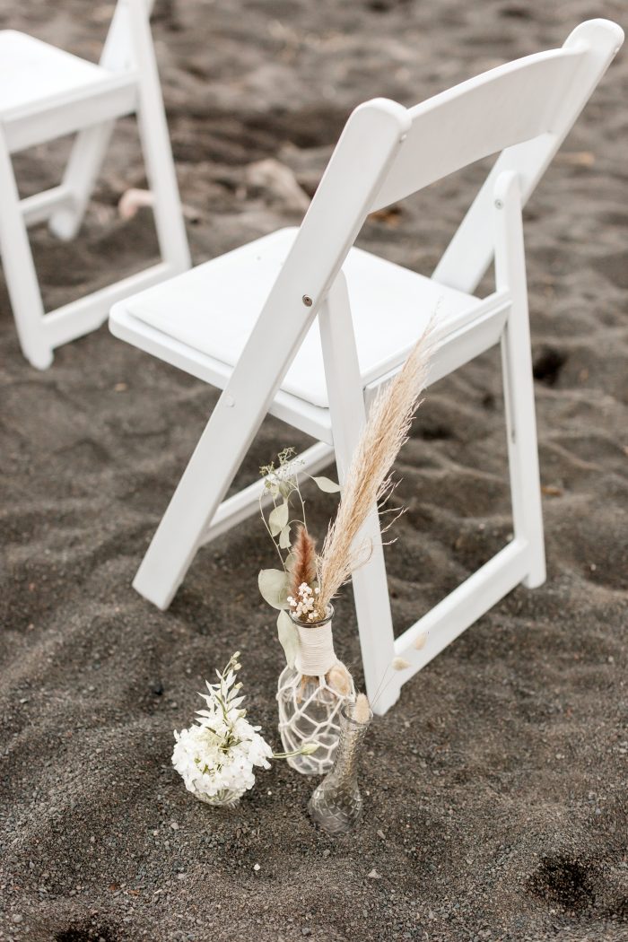 Flowers Next to White Chair on Black Sand Beach at Beach Elopement Ceremony