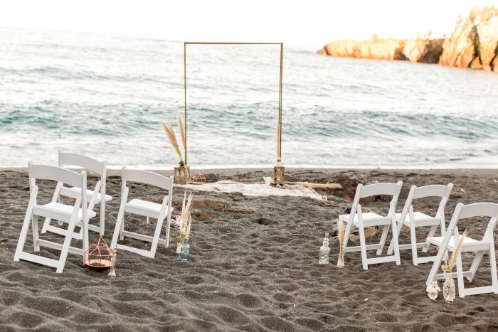 Wedding Arch Surrounded by White Chairs on Black Sand Beach or Beach Elopement