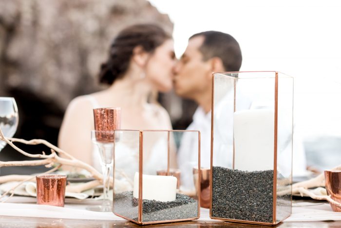 Bride and Groom Kissing Behind Sweetheart Table Featuring Little Wedding Details for Beach Elopement