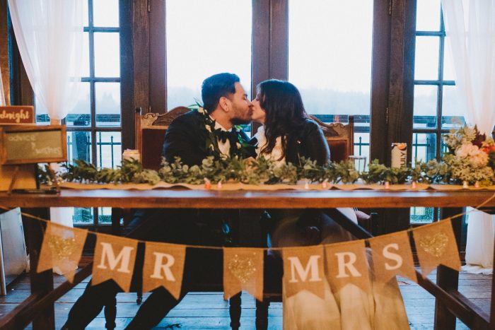Bride and Groom Kissing While Sitting at Table with DIY Mr. and Mrs. Sign