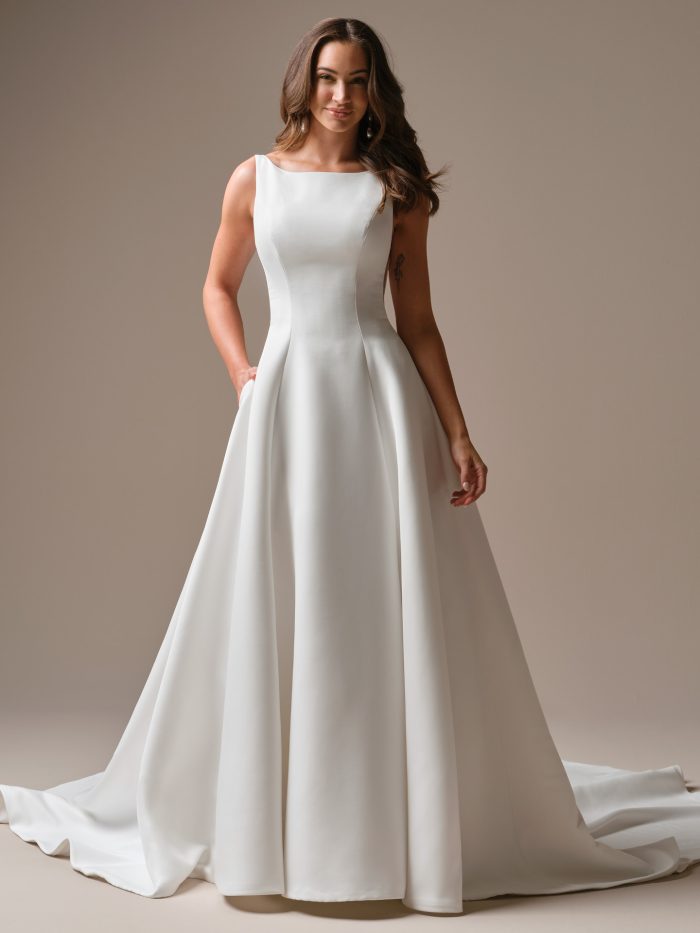 Minimal satin A-line wedding dress with bateau neckline, tank straps, clean silhouette, and chapel train with pockets.