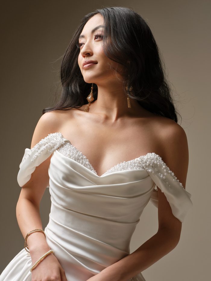 Satin basque waist ballgown wedding dress with strapless draped bodice, pearl-accented neckline, and voluminous skirt with pockets.