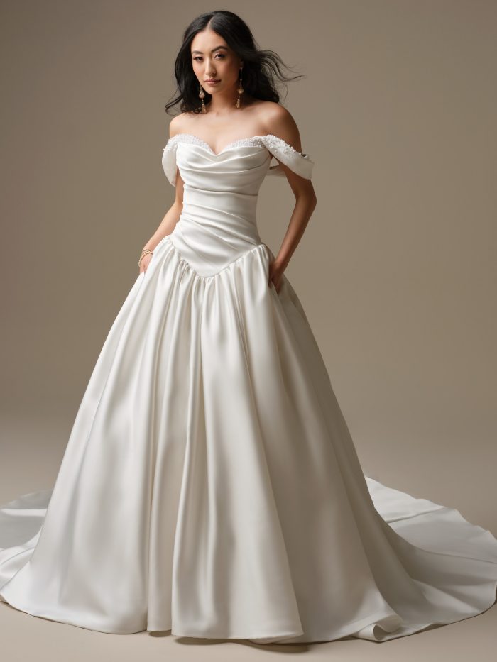 Close-up of satin ballgown wedding dress with draped sweetheart neckline, pearl-accented trim, and off-the-shoulder sleeves.