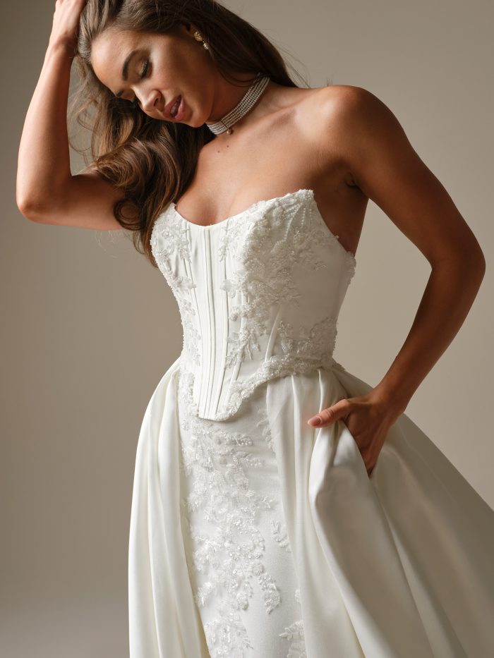Close-up of strapless mock two-piece wedding dress with structured corset bodice, lace appliqué detail, and soft draped overskirt.