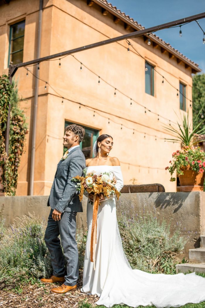 Groom Standing in Front of Tuscan Villa Wedding Venue with Real Bride Wearing Modern Crepe Wedding Dress Called Admina by Maggie Sottero
