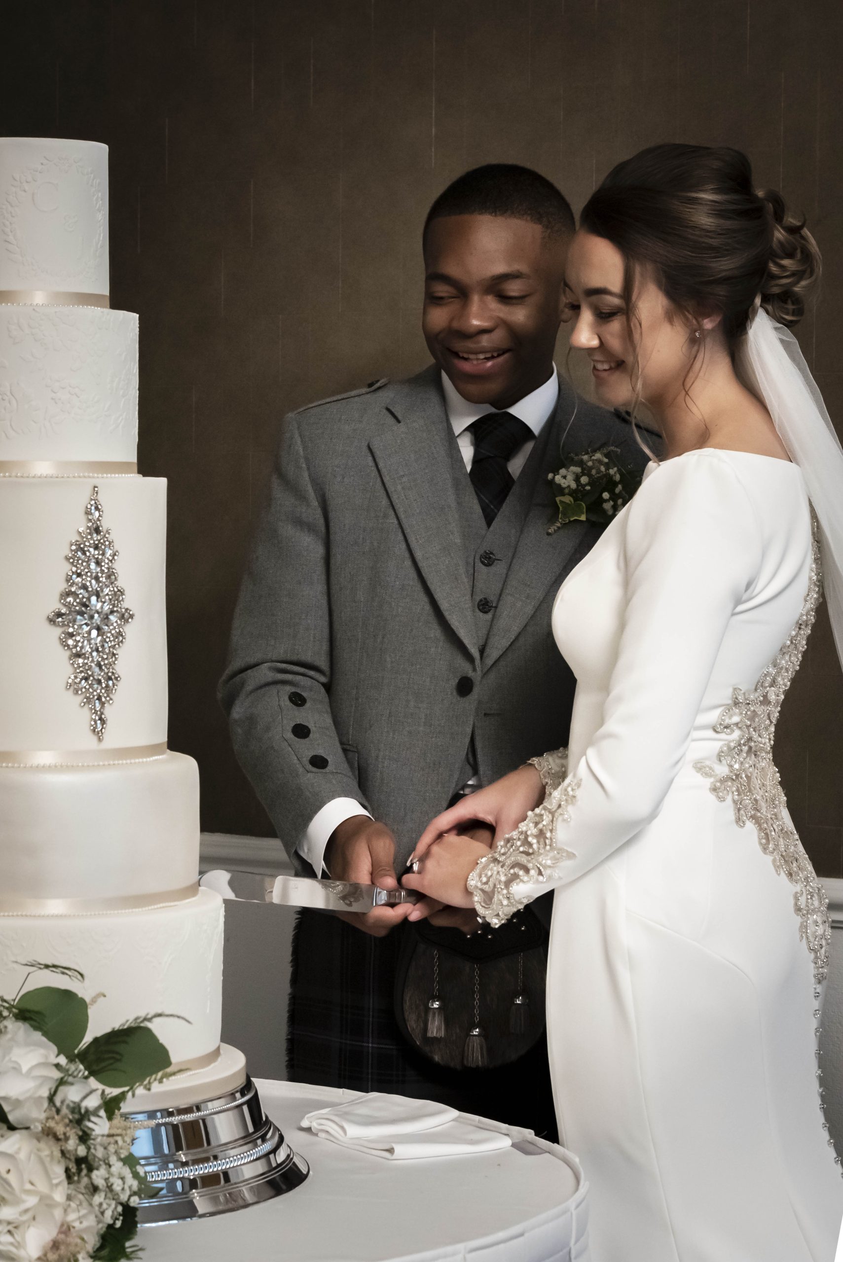 Mariée debout à côté du marié et du gâteau de mariage vêtue d'une robe appelée Aston par Sottero & Midgley