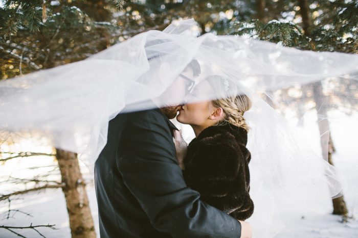 Groom And Bride Kissing Under Veil With Bride Wearing Fur Coat Wearing A Dress Called Allen By Sottero And Midgley