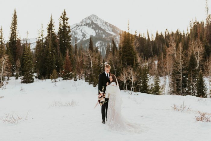 Groom in Winter Mountain Landscape with Real Bride Wearing a Fur Wrap and Modest Maggie Sottero Wedding Dress