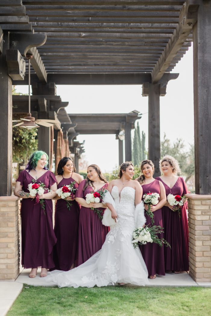 Bride Posing With Bridesmaids Wearing Maroon Gowns With Bride Wearing A Wedding Gown Called Hattie By Rebecca Ingram