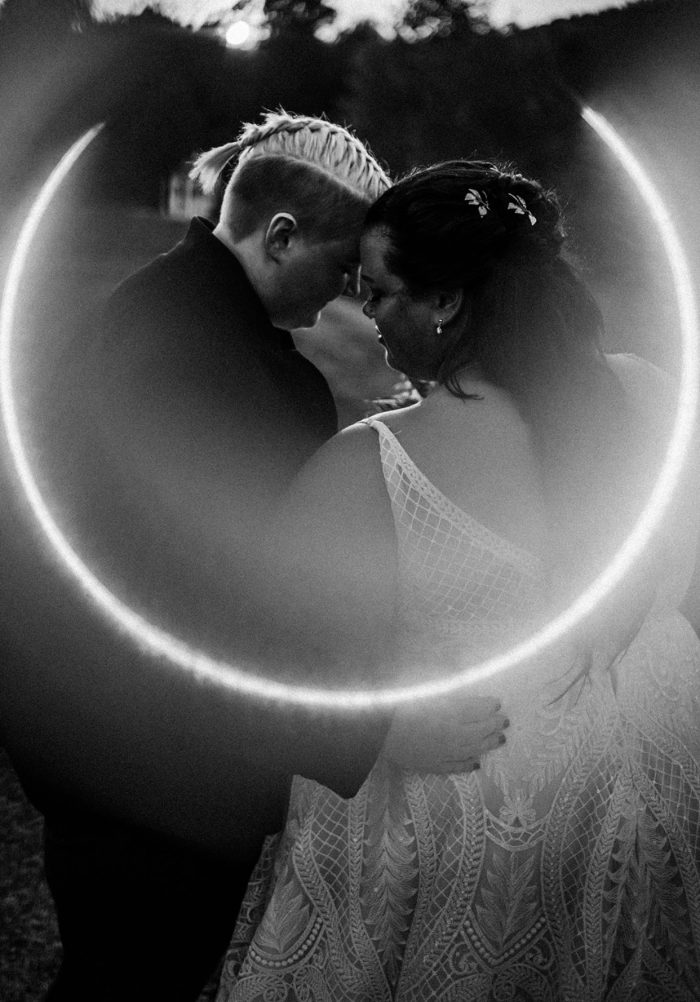 Bride Standing With Partner In Black And White Photo With Unique Lighting With Bride Wearing A Wedding Gown Called Roxanne By Sottero And Midgley