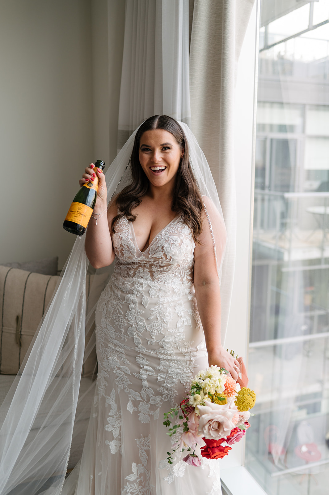 Comment acheter une robe de mariée avec la mariée célébrant dire oui à la robe tenant une bouteille de champagne avec la mariée portant une robe de mariée appelée Greenley par Maggie Sottero