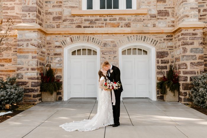 Groom Kissing Bride Wearing Modest Lace Sheath Wedding Dress Called Tuscany Leigh by Maggie Sottero