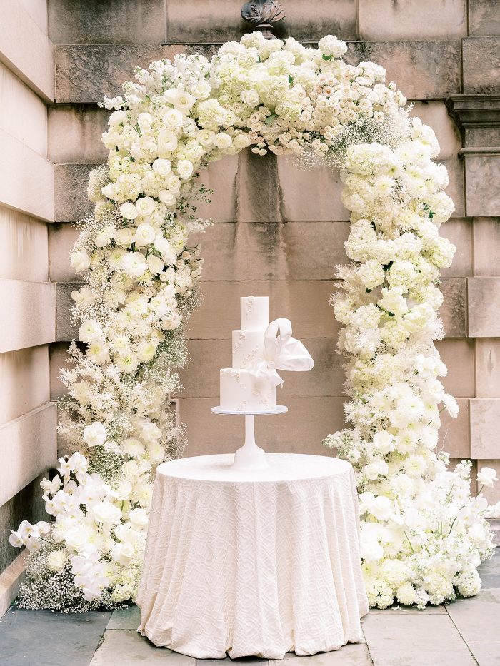 White floral arch with a white royal inspired cake inside