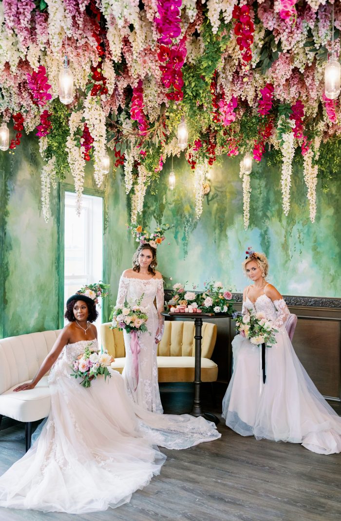Three models wearing fun floral headpieces while wearing Maggie Sottero wedding dresses surrounded by pink and white flowers