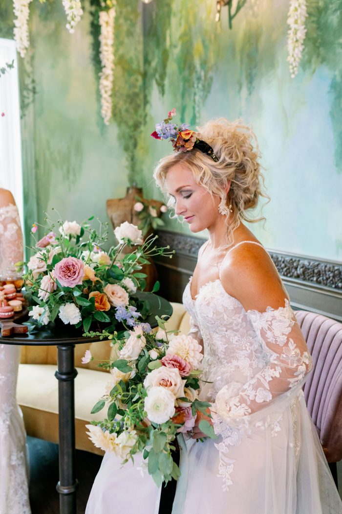 Model wearing Stevie Long Sleeve a-line wedding dress by Maggie Sottero while holding pastel florals and greenery